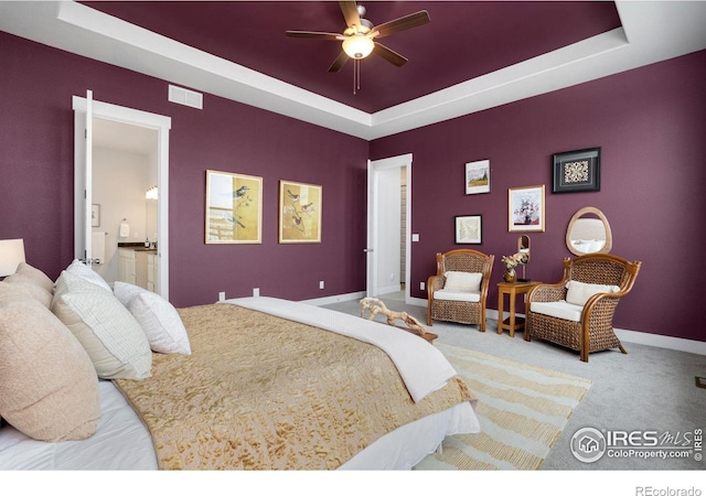 bedroom featuring ensuite bath, a tray ceiling, and carpet flooring