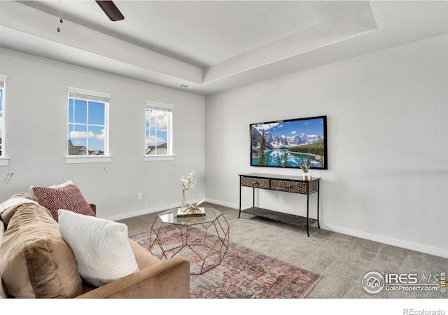 living room with a raised ceiling, carpet, and ceiling fan