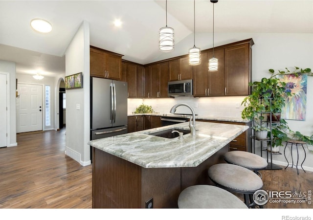 kitchen featuring stainless steel appliances, sink, vaulted ceiling, light stone counters, and pendant lighting