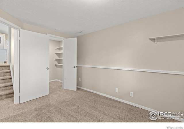 unfurnished bedroom with a closet, carpet flooring, a textured ceiling, and a spacious closet