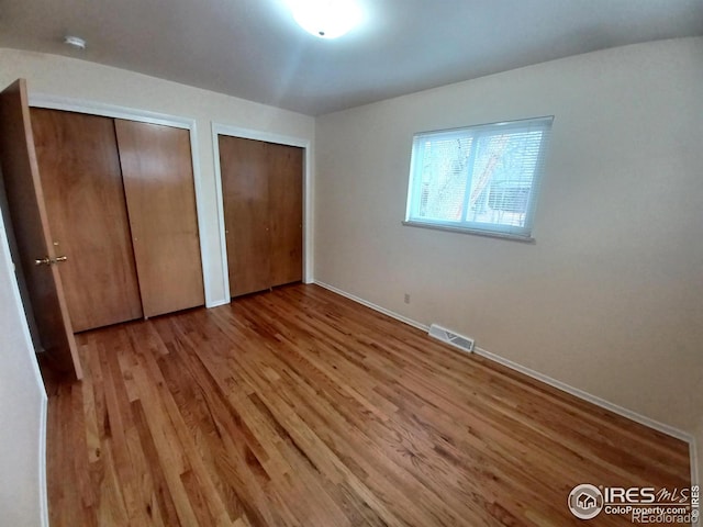 unfurnished bedroom with two closets and light wood-type flooring