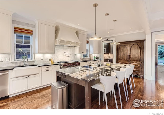 kitchen featuring sink, custom range hood, hanging light fixtures, a center island with sink, and appliances with stainless steel finishes