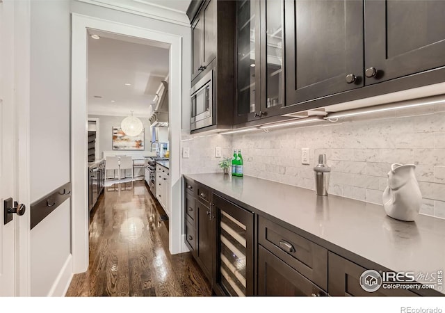 bar featuring stainless steel microwave, beverage cooler, dark hardwood / wood-style flooring, and dark brown cabinetry