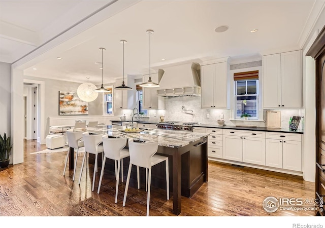 kitchen featuring a center island, custom range hood, backsplash, white cabinetry, and dark stone countertops