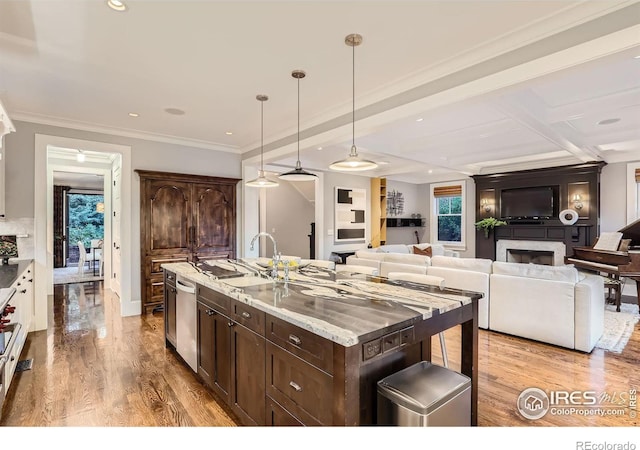 kitchen with a kitchen island with sink, hanging light fixtures, dark brown cabinetry, sink, and stainless steel dishwasher