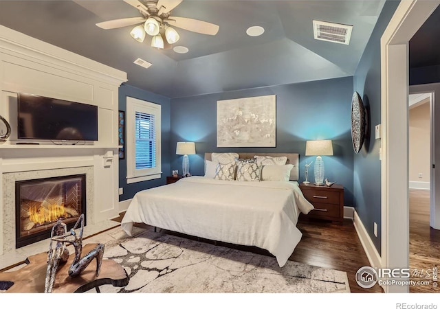 bedroom with vaulted ceiling, a raised ceiling, ceiling fan, dark wood-type flooring, and a fireplace