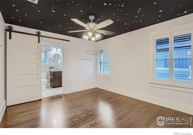 empty room featuring ceiling fan, a barn door, and hardwood / wood-style flooring