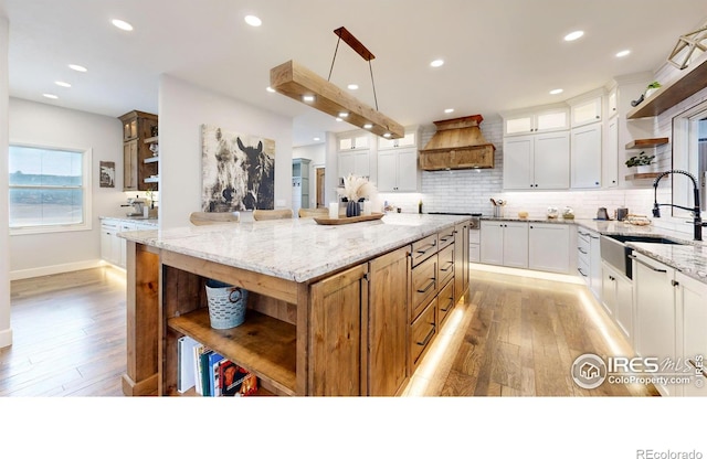 kitchen with light stone counters, white cabinets, custom exhaust hood, and sink