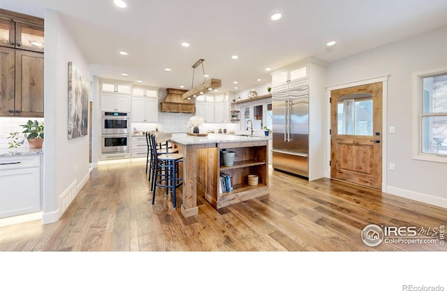 kitchen featuring decorative light fixtures, white cabinets, a large island, tasteful backsplash, and appliances with stainless steel finishes