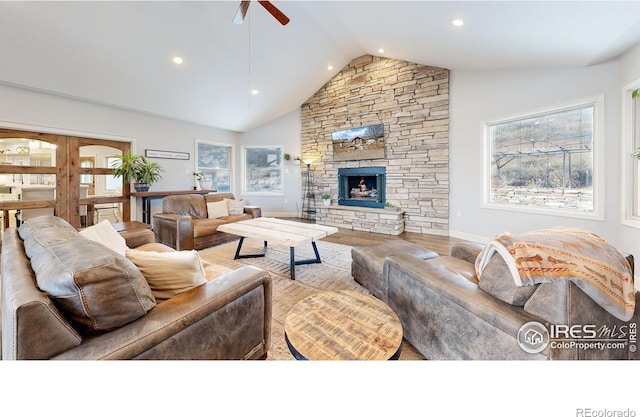 living room featuring lofted ceiling, ceiling fan, and a stone fireplace