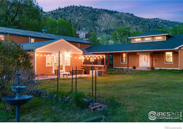 back house at dusk with a yard, a mountain view, and a patio area