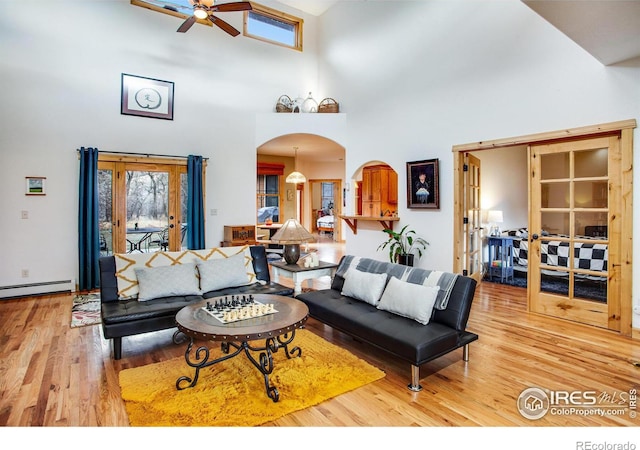 living room with a towering ceiling, french doors, light wood-type flooring, ceiling fan, and a baseboard radiator