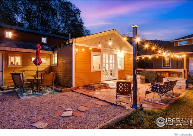 back house at dusk featuring french doors, a fire pit, an outdoor structure, and a patio