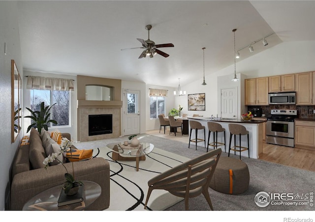 living room featuring ceiling fan with notable chandelier, a fireplace, and vaulted ceiling