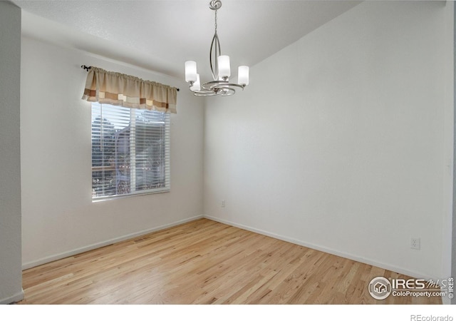 empty room featuring light wood-type flooring and an inviting chandelier