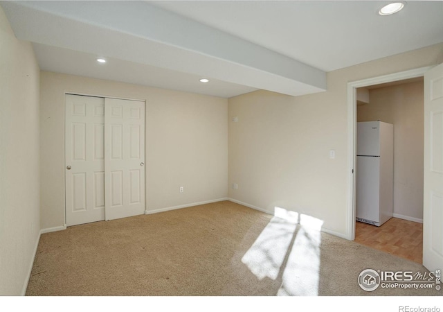 unfurnished bedroom with light carpet, a closet, and white refrigerator