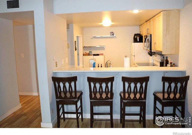 kitchen featuring white cabinets, white fridge, a breakfast bar area, range, and dark wood-type flooring