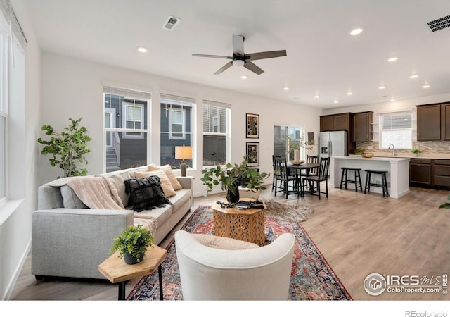 living room featuring light hardwood / wood-style floors, ceiling fan, and a healthy amount of sunlight