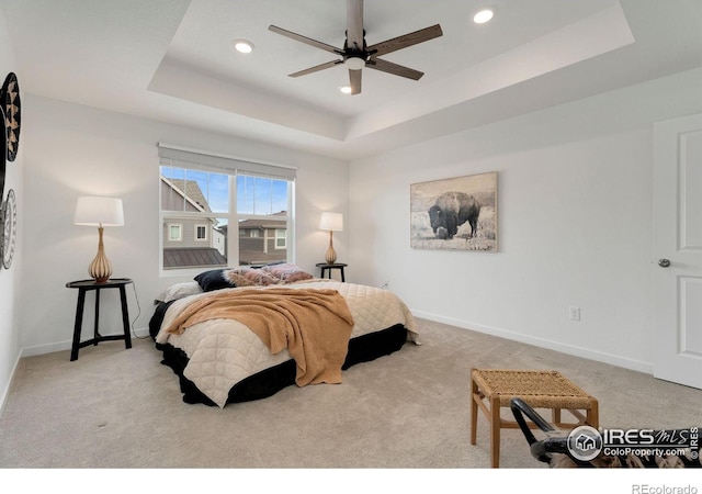 carpeted bedroom with a raised ceiling and ceiling fan