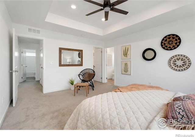 carpeted bedroom with a raised ceiling, connected bathroom, and ceiling fan