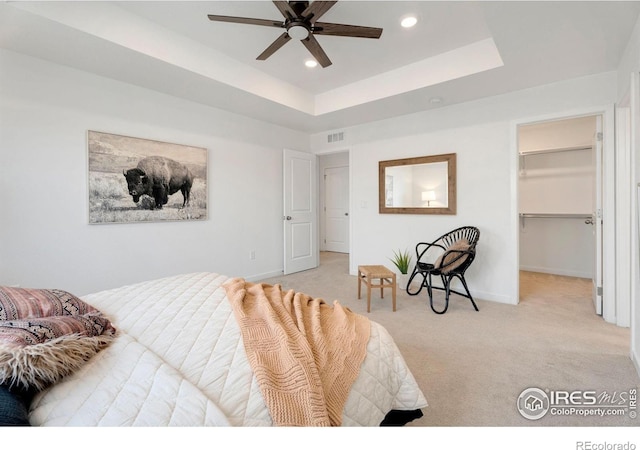 bedroom featuring a spacious closet, light carpet, ceiling fan, a closet, and a tray ceiling