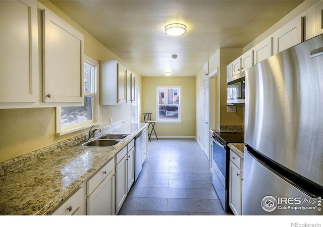 kitchen featuring appliances with stainless steel finishes, white cabinetry, light stone countertops, and sink