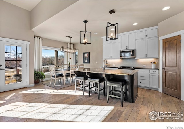 kitchen featuring white cabinetry, light wood-type flooring, pendant lighting, backsplash, and a kitchen island with sink