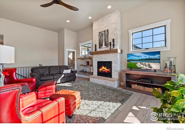 living room with hardwood / wood-style floors, ceiling fan, and a stone fireplace