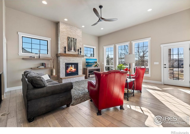 living room featuring ceiling fan, light hardwood / wood-style floors, and a stone fireplace