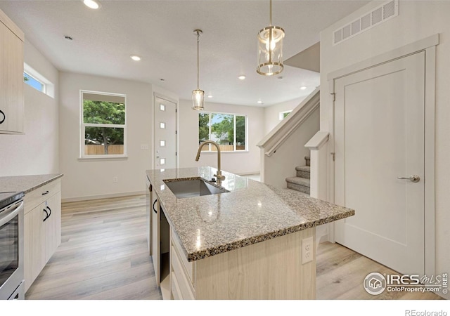 kitchen featuring light stone counters, a wealth of natural light, decorative light fixtures, a kitchen island with sink, and sink