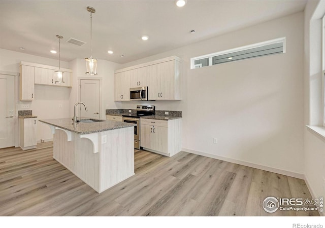 kitchen with light stone countertops, hanging light fixtures, a center island with sink, appliances with stainless steel finishes, and sink