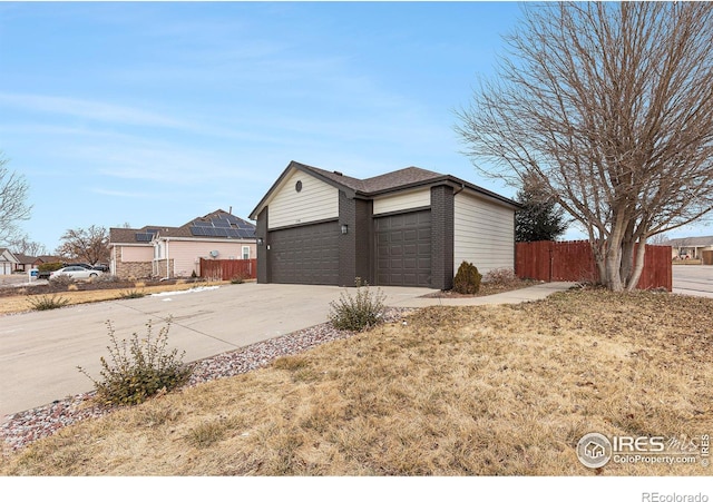 view of property exterior featuring brick siding, an attached garage, driveway, and fence