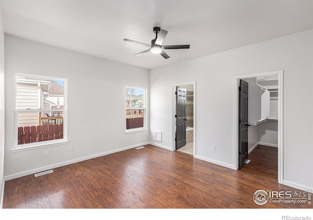 unfurnished bedroom with a walk in closet, multiple windows, wood finished floors, and visible vents