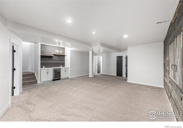 unfurnished living room with a bar, beverage cooler, visible vents, and light carpet