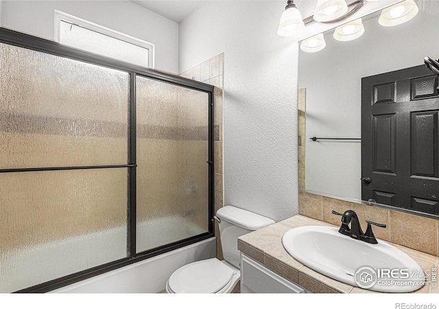 full bath with vanity, toilet, a textured wall, and combined bath / shower with glass door