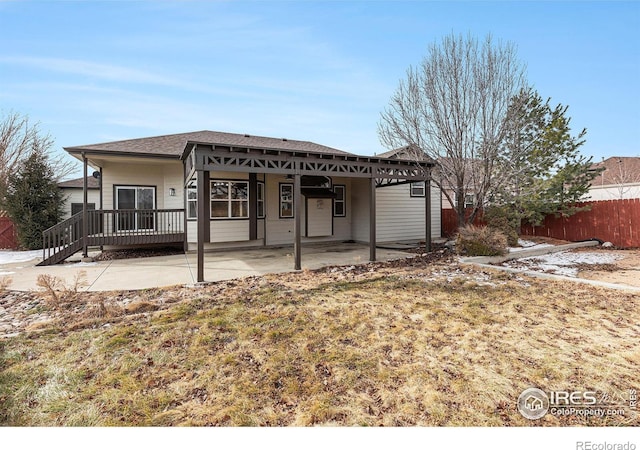 rear view of property featuring fence, roof with shingles, and a patio area