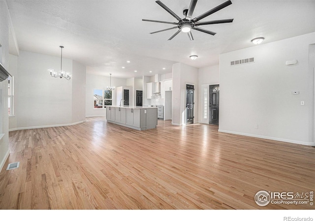 unfurnished living room with visible vents, light wood finished floors, baseboards, and ceiling fan with notable chandelier