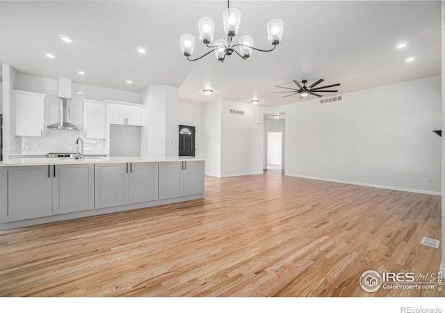 kitchen with light wood-type flooring, visible vents, ceiling fan with notable chandelier, wall chimney range hood, and light countertops