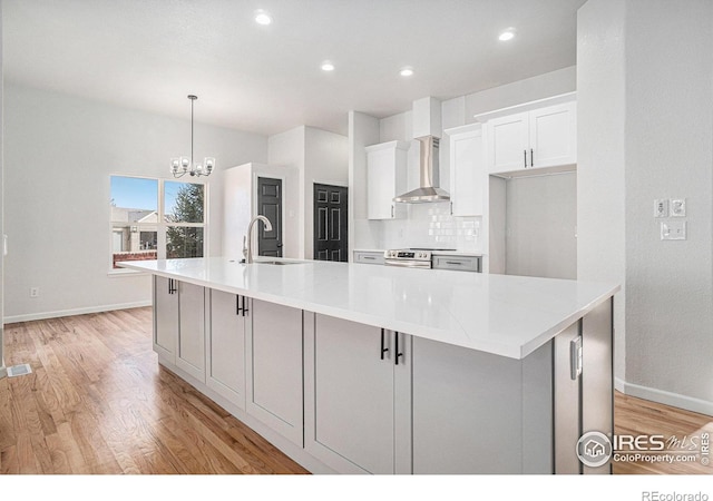 kitchen featuring electric range, a large island, a sink, an inviting chandelier, and wall chimney range hood