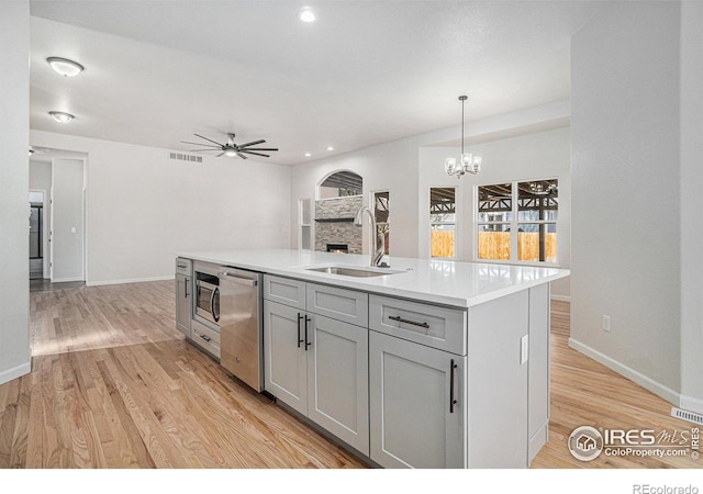 kitchen with a sink, light wood-type flooring, appliances with stainless steel finishes, and ceiling fan with notable chandelier