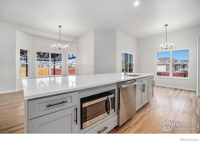 kitchen with a sink, light wood finished floors, appliances with stainless steel finishes, and an inviting chandelier