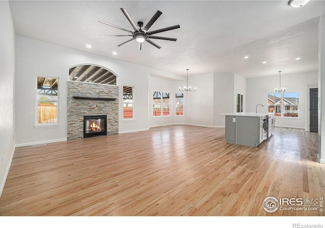 unfurnished living room featuring light wood-type flooring, a stone fireplace, ceiling fan with notable chandelier, a textured ceiling, and a sink