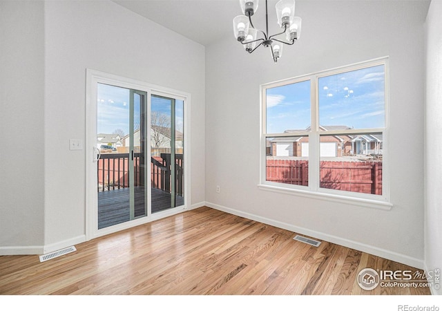 spare room with a notable chandelier, baseboards, visible vents, and light wood finished floors