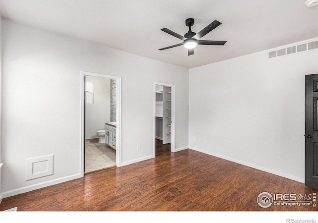 unfurnished bedroom with visible vents, baseboards, a walk in closet, and wood finished floors