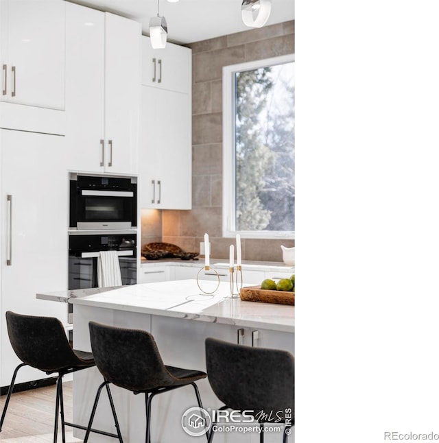 kitchen featuring light stone countertops, white cabinets, tasteful backsplash, light hardwood / wood-style floors, and a breakfast bar area