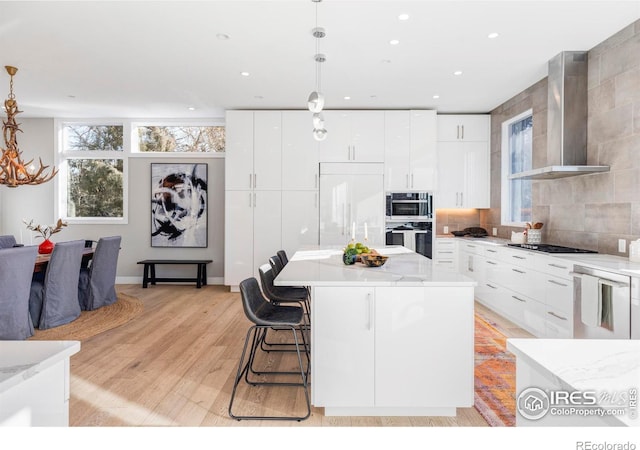 kitchen featuring decorative light fixtures, white cabinets, and wall chimney range hood