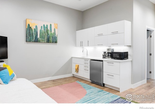 kitchen featuring sink, white cabinetry, light hardwood / wood-style flooring, and stainless steel refrigerator