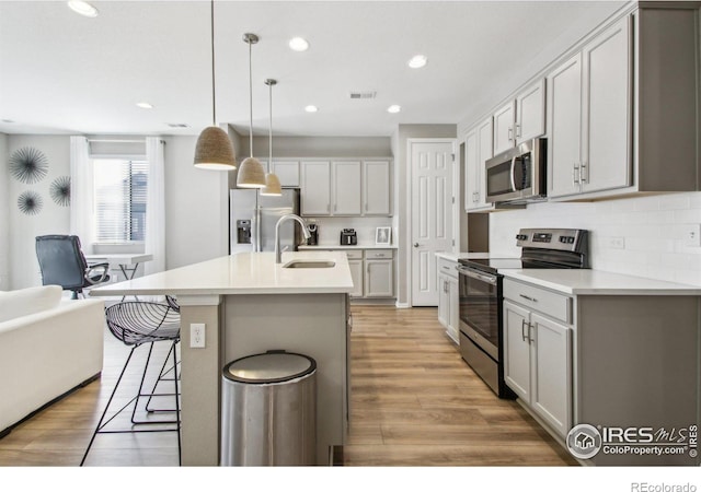 kitchen featuring sink, decorative light fixtures, tasteful backsplash, a center island with sink, and appliances with stainless steel finishes