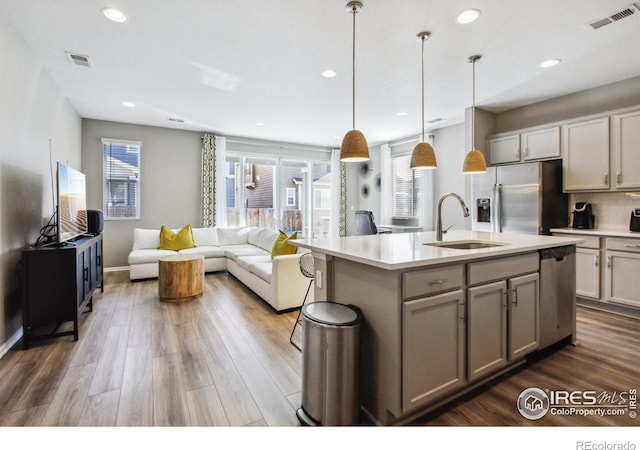 kitchen featuring decorative light fixtures, stainless steel appliances, a kitchen island with sink, gray cabinets, and sink