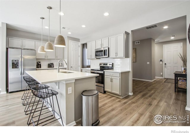 kitchen with sink, decorative light fixtures, backsplash, a kitchen island with sink, and appliances with stainless steel finishes